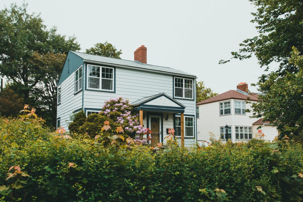 Charming two-story wooden house surrounded by lush greenery and vibrant flowers in a suburban neighborhood.